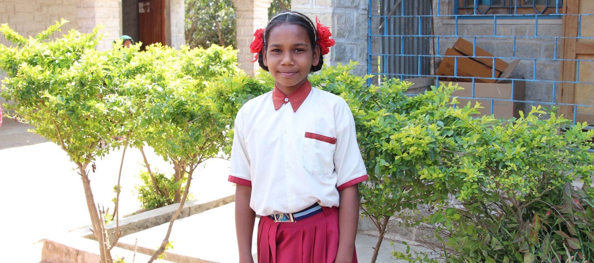 Flicka i skoluniform framför skolbyggnad i Indien.